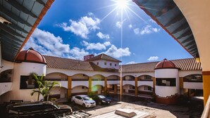 A courtyard with a clear blue sky, a sun shining through an archway, and a building with a tiled roof and multiple balconies. - Del Mar Inn Playas de Tijuana (Tijuana)