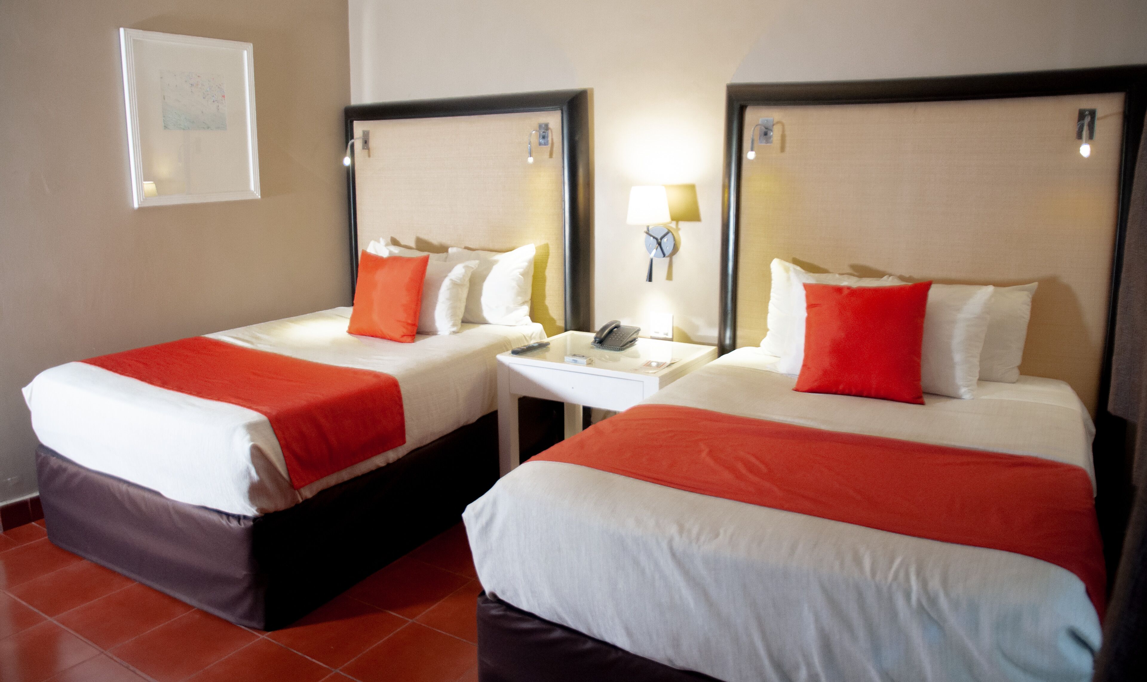 A hotel room with two beds, each with a red blanket, white linens, and a nightstand with a lamp and phone.