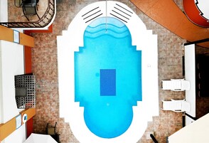 Vista desde arriba de una piscina con centro azul, rodeada por una terraza blanca.