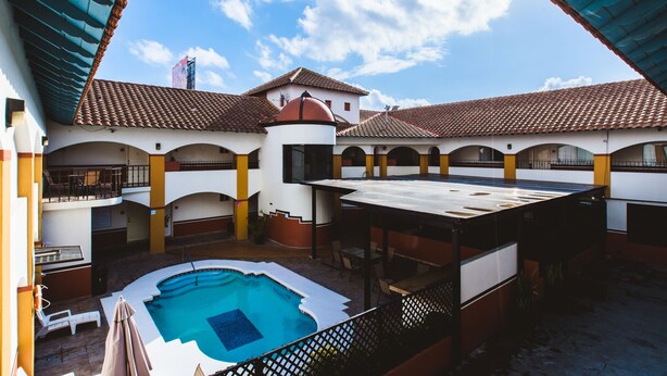A courtyard with a swimming pool, covered seating areas, and a building with a tiled roof and arches. - Del Mar Inn Playas de Tijuana (Tijuana)