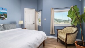 Ein Schlafzimmer mit Bett, Stuhl, Fenster und einer Zimmerpflanze.