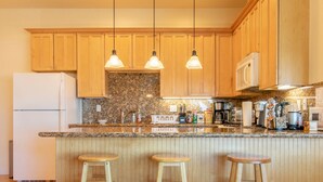 A kitchen with wooden cabinets, a granite countertop, a white refrigerator, and three bar stools.
