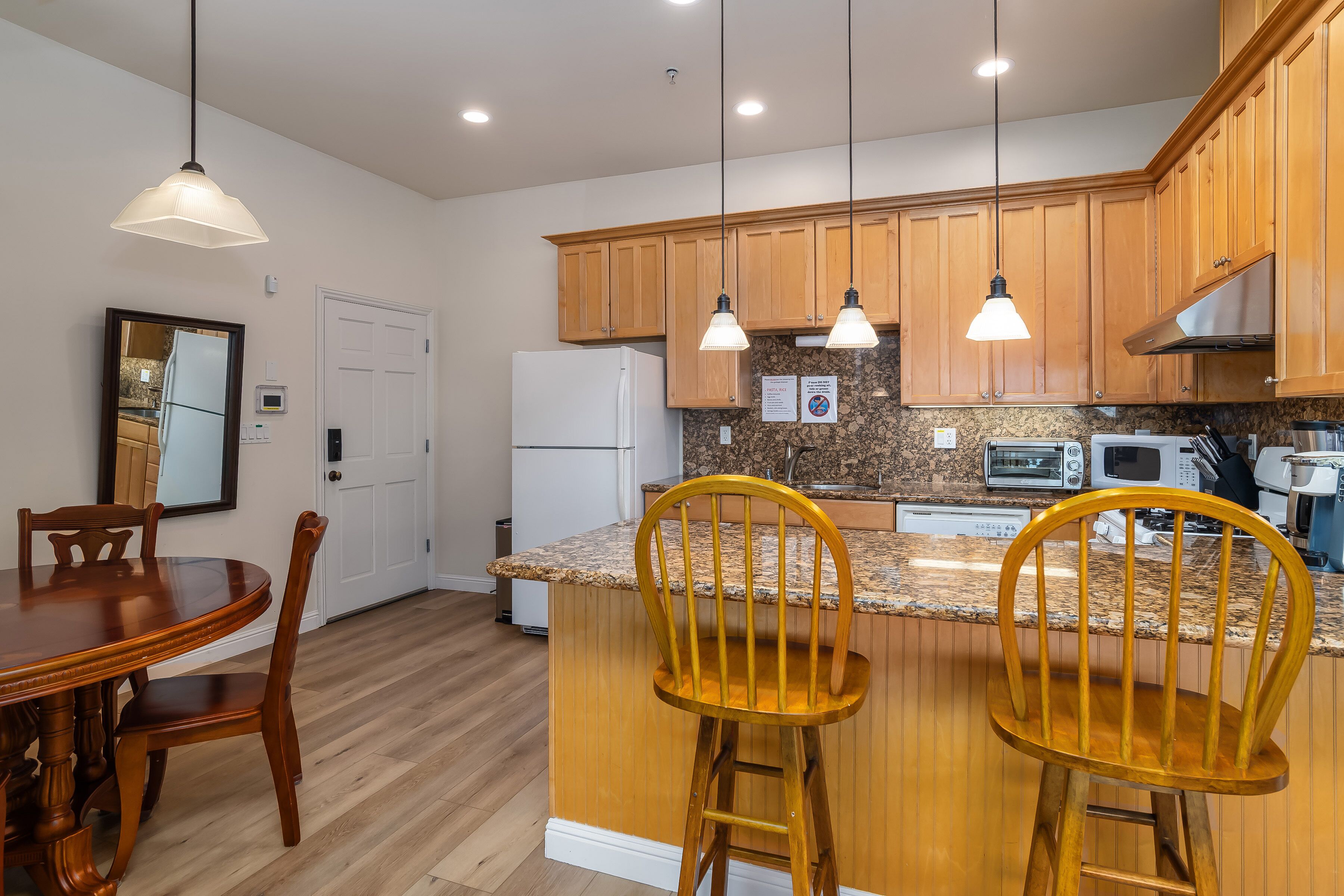 A modern kitchen with wooden cabinets, a granite countertop, and pendant lighting.