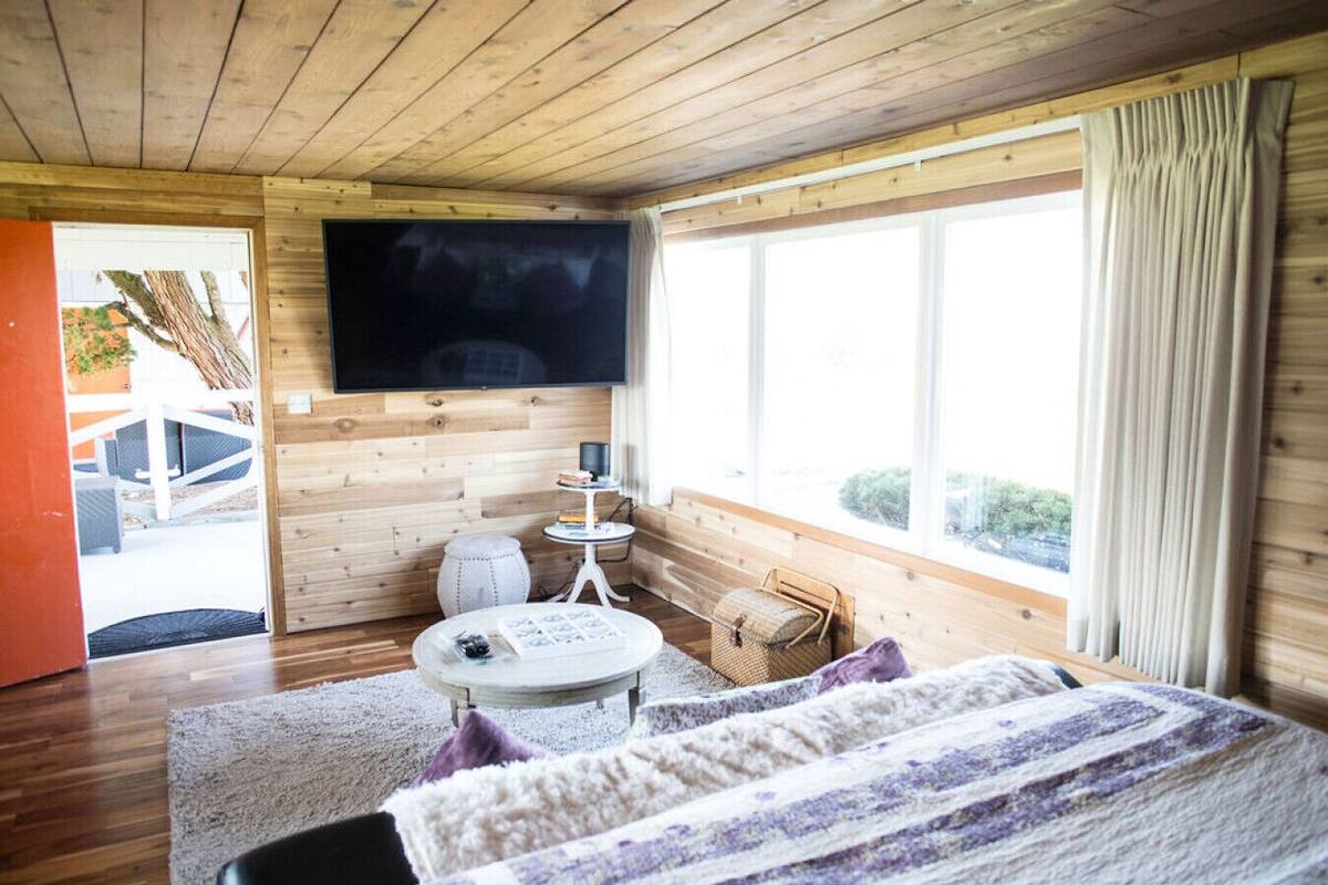A wooden-paneled room with a bed, a TV, a small table, and a window.