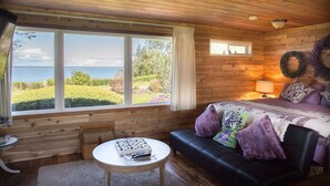 Una habitación de cabaña acogedora con un ventanal grande que ofrece vistas panorámicas, una cama cómoda, una mesita pequeña y un sofá de cuero.
