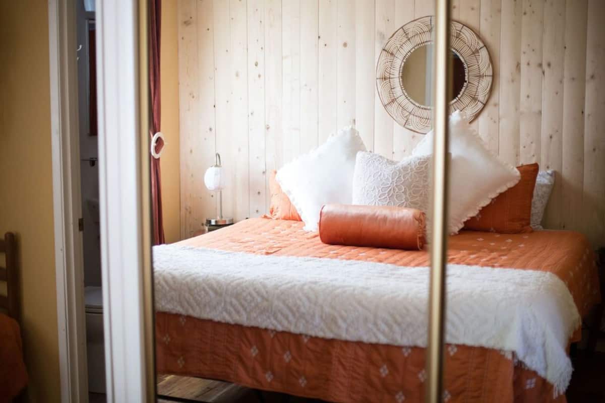 A bedroom with a bed, pillows, a mirror, and a wall-mounted light fixture.
