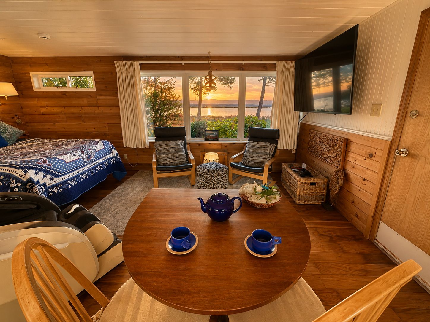 A cozy room with a bed, two chairs, a table with a teapot and cups, and a window with a view.