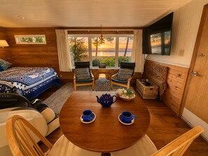 A cozy room with a bed, two chairs, a table with a teapot and cups, and a window with a view. - Dungeness Bay Cottages (Sequim)