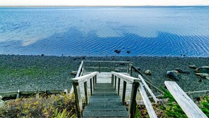 Una escalera de madera que desciende hacia una costa rocosa, con vistas al océano.