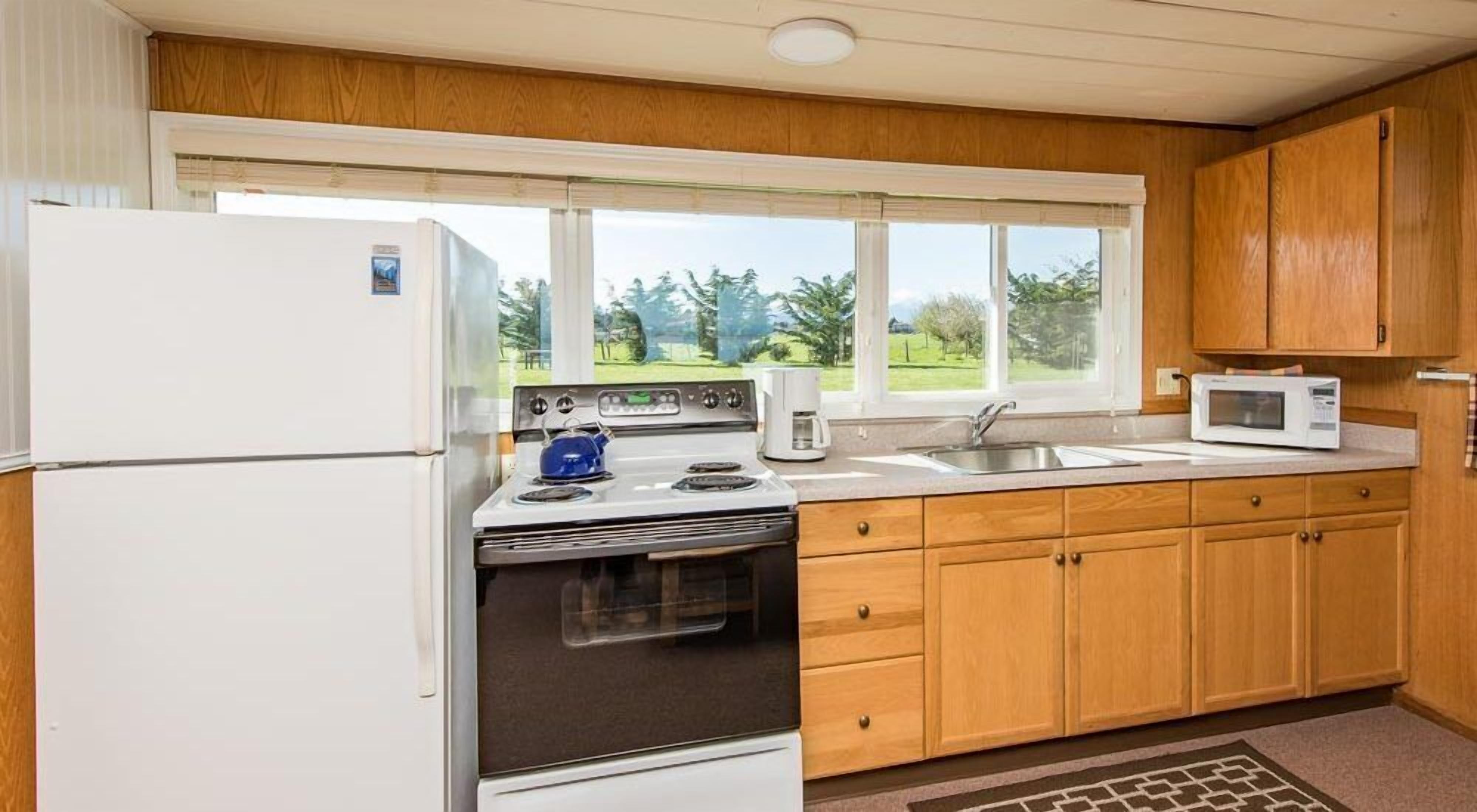 Cocina pequeña con refrigerador, estufa, microondas y armarios de madera.