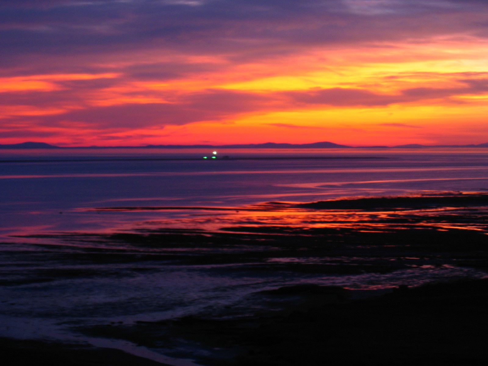 A sunset over a body of water with distant landforms.