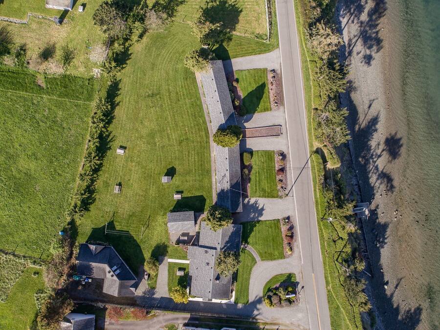 An aerial view of a residential area with a house, a driveway, and a body of water.