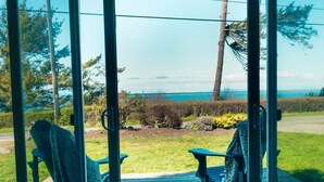 Una terraza con dos sillas Adirondack mirando hacia un área verde y vistas al océano.