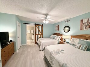 Ein Schlafzimmer mit zwei Betten, einem Deckenventilator, einem Fernseher und einer Holzkommode.