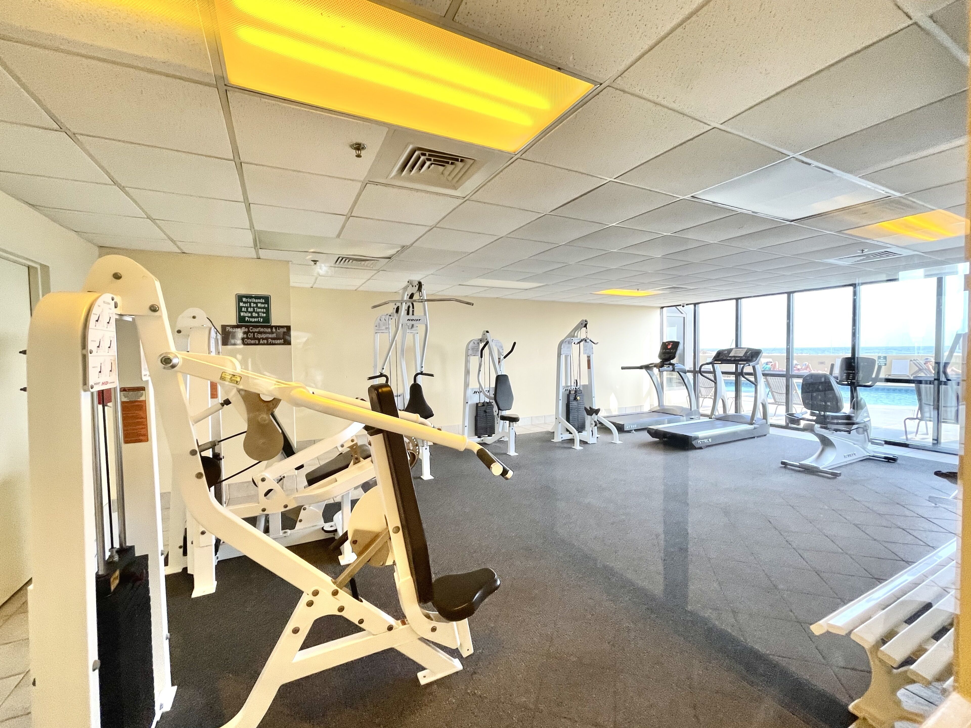 Ein Fitnessstudio mit unterschiedlichen Trainingsgeräten, einem Laufband und Blick auf den Strand durch große Fenster.