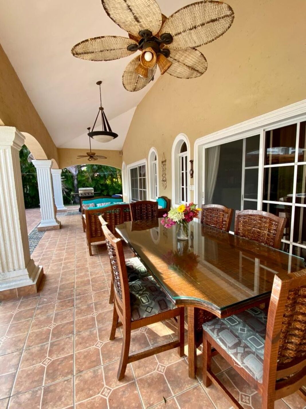 A spacious patio with a long dining table, wicker chairs, and a ceiling fan.