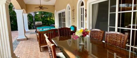 A spacious patio with a long dining table, wicker chairs, and a ceiling fan.
