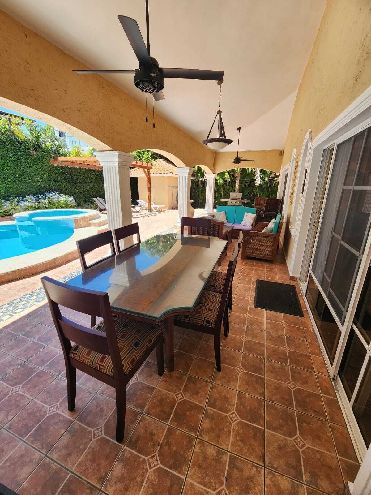 Een terras buiten met een eettafel, stoelen en een plafondventilator.