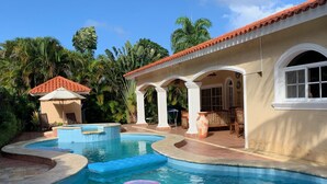 Ein Swimmingpool mit Whirlpool, Palmen und einer überdachten Terrasse.