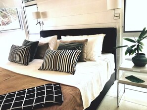 A modern bedroom with a large bed, multiple pillows, a bedside table with a plant, and a window with natural light. - ★Luxury Apartment in Gated Eco-Community. 1min walk to the Beach★ (Santa Teresa Beach)