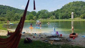 Eine Uferlandschaft mit Wassersportlern, einer Hängematte und verschiedenen Strandgegenständen.