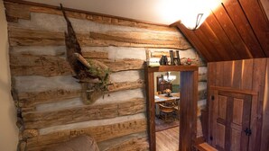 Ein rustikaler Innenraum mit einer Wand aus Holzbalken, einem Spiegel, der einen Essbereich reflektiert, und einer Holztür.