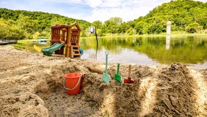Ein Sandstrand mit einer hölzernen Spielkonstruktion und einem kleinen Boot im Wasser.