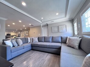 A modern living room with a sectional sofa, recessed ceiling lights, and a kitchen in the background. - Stunning Pool/Jac Home: 5 EnSuites & Game Room (Anaheim)