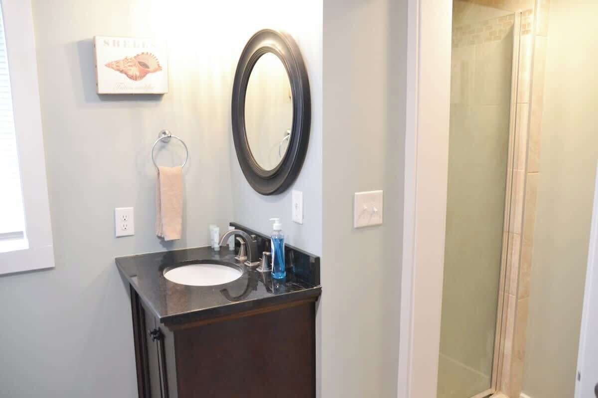 A bathroom with a black sink, a mirror, a towel rack, and a shower area.