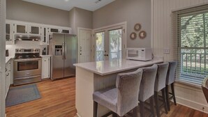 A modern kitchen with white cabinetry, stainless steel appliances, and a central island with bar stools. - Award-Winning Resort Amenities | Grand Pavilion 76 (Isle of Palms)