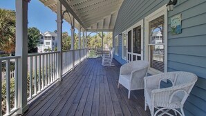 A covered porch with white wicker furniture and a view of neighboring houses. - Award-Winning Resort Amenities | Grand Pavilion 76 (Isle of Palms)