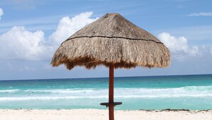 A beach umbrella on a sandy beach with the ocean in the background. - Affordable Cancun Oceanfront Condo at the "Zona Hotelera" Hotel Zone (Cancun)