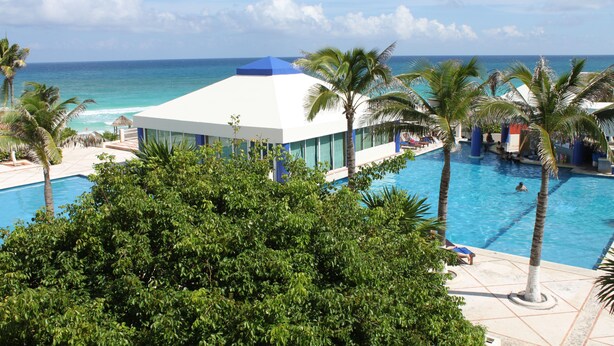 A resort with a pool, palm trees, and a view of the ocean. - Affordable Cancun Oceanfront Condo at the "Zona Hotelera" Hotel Zone (Cancun)