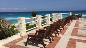 A row of wooden chairs facing a beach with a clear view of the ocean. - Affordable Cancun Oceanfront Condo at the "Zona Hotelera" Hotel Zone (Cancun)