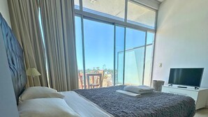 A modern bedroom with a large bed, a TV, and a view of the outdoors. - Departamento Alassio (Tigre)