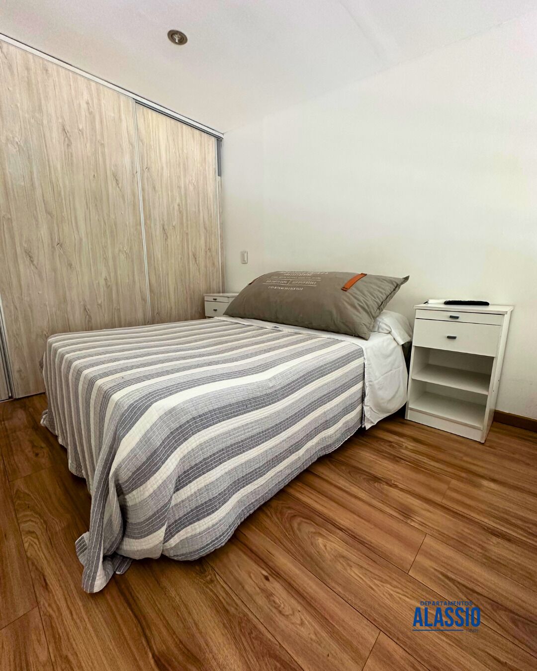 Un dormitorio con cama, mesita de noche, armario y suelo de madera.