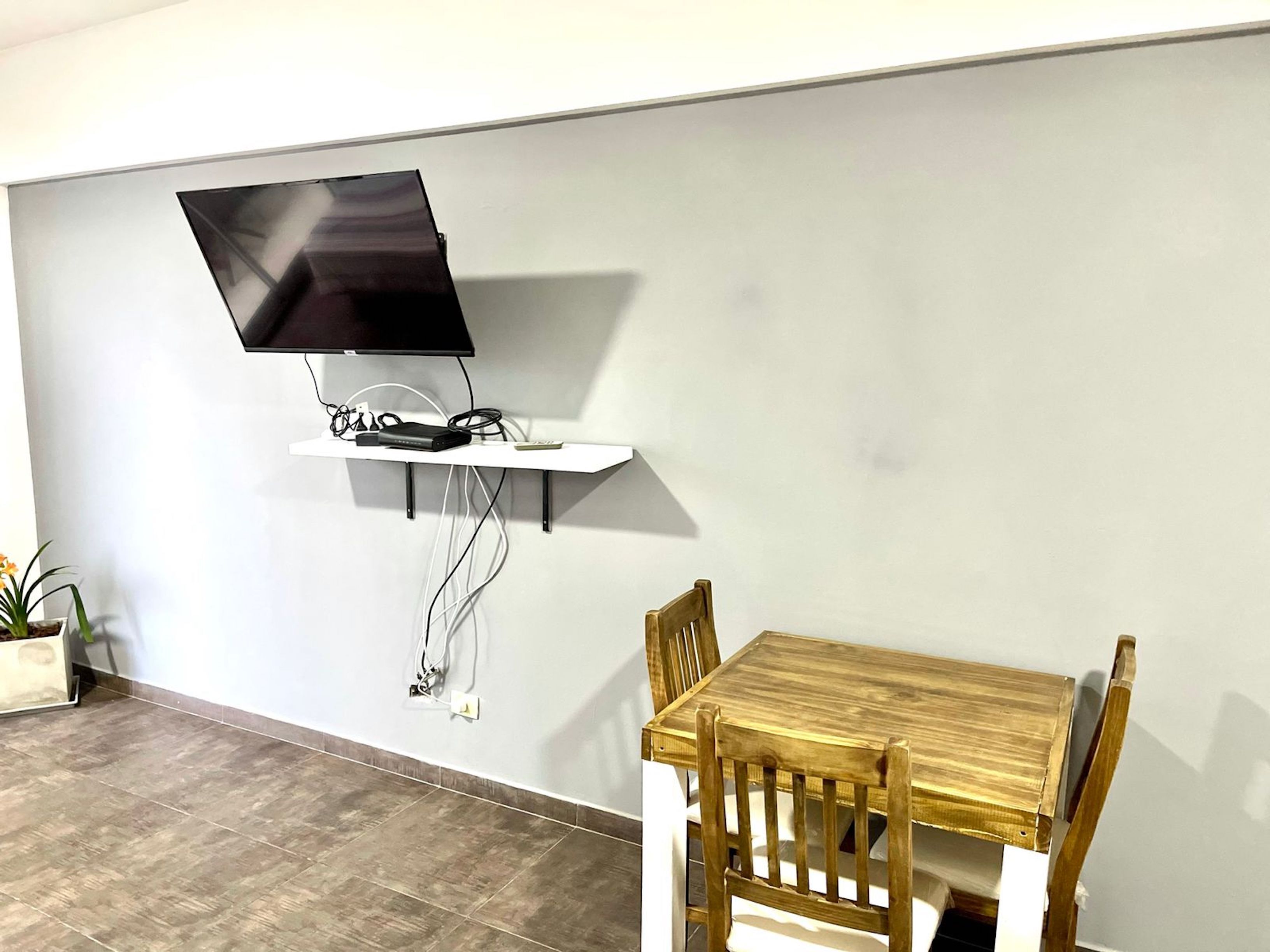 Ein modernes Zimmer mit einem an der Wand befestigten Fernseher auf einem weißen Regal, einem Holztisch und einem Stuhl.
