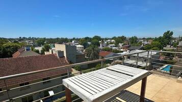 Una terraza en la azotea con barandilla metálica, un banco de madera y vistas a una zona residencial.
