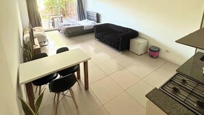 A compact living space with a dining area, a sofa, a small kitchen, and a balcony with a view of the outdoors. - Departamento Alassio (Tigre)