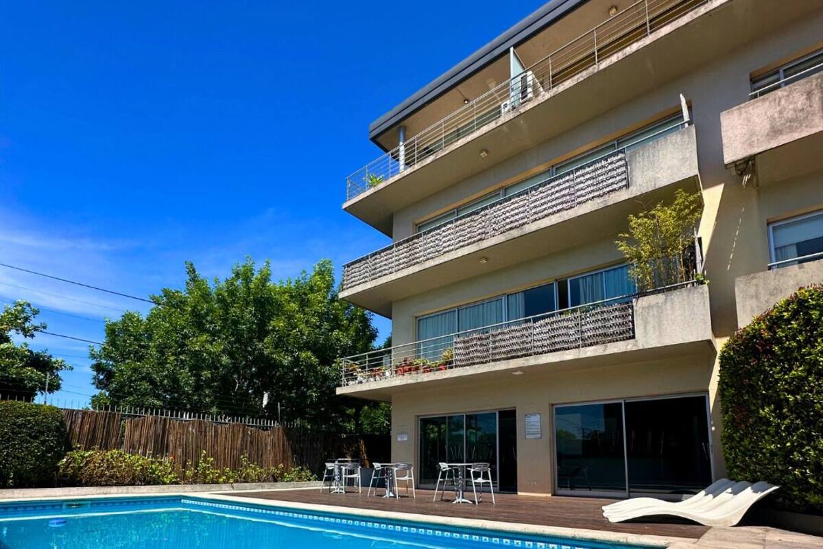 A modern apartment building with a swimming pool, outdoor seating, and a wooden fence.