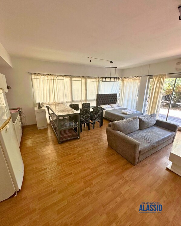 Uma sala de estar moderna com um sofá, uma mesa de jantar com cadeiras e uma área de cozinha com geladeira e cafeteira.