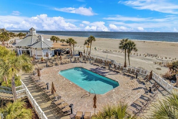 A pool area with lounge chairs and umbrellas, a gazebo, and a view of the beach.