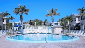 A pool area with lounge chairs and palm trees, surrounded by buildings.