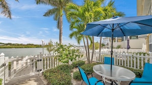 A patio with a table and chairs, a white picket fence, and palm trees.