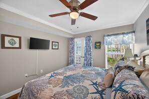 Ein Schlafzimmer mit Bett, Deckenventilator, Fernseher und einem Fenster mit Vorhängen.