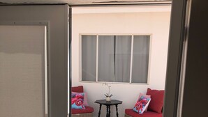 Une porte coulissante s’ouvre sur un patio aménagé avec deux canapés en osier, une petite table et un pot de fleurs.