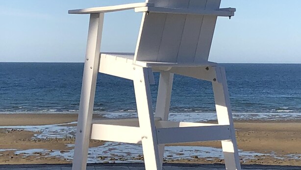 Une chaise Adirondack blanche, placée sur un chemin pavé, au bord de la plage.
