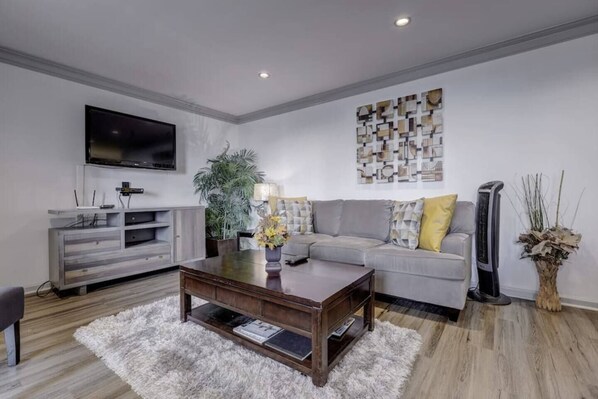 Una sala de estar moderna con un sofá gris, una mesa de centro, un televisor, un mueble gris y un adorno de pared.