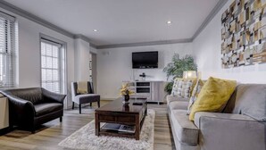 A modern living room with a sofa, armchair, coffee table, and a TV mounted on the wall.