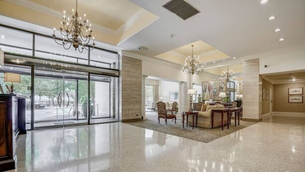 A spacious lobby with a polished floor, a reception desk, a seating area with a sofa and chairs, and a chandelier.